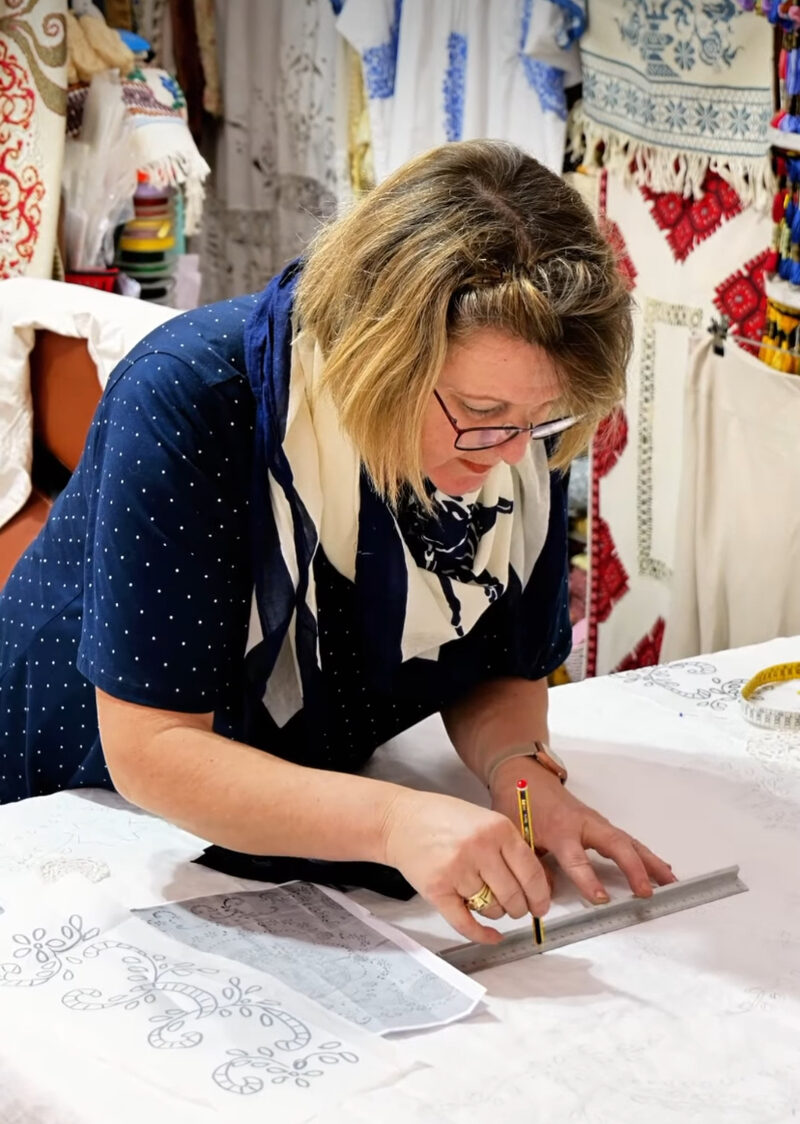 Antonia, master embroiderer, drawing embroidery patterns with ruler and pencil in her Athens workshop